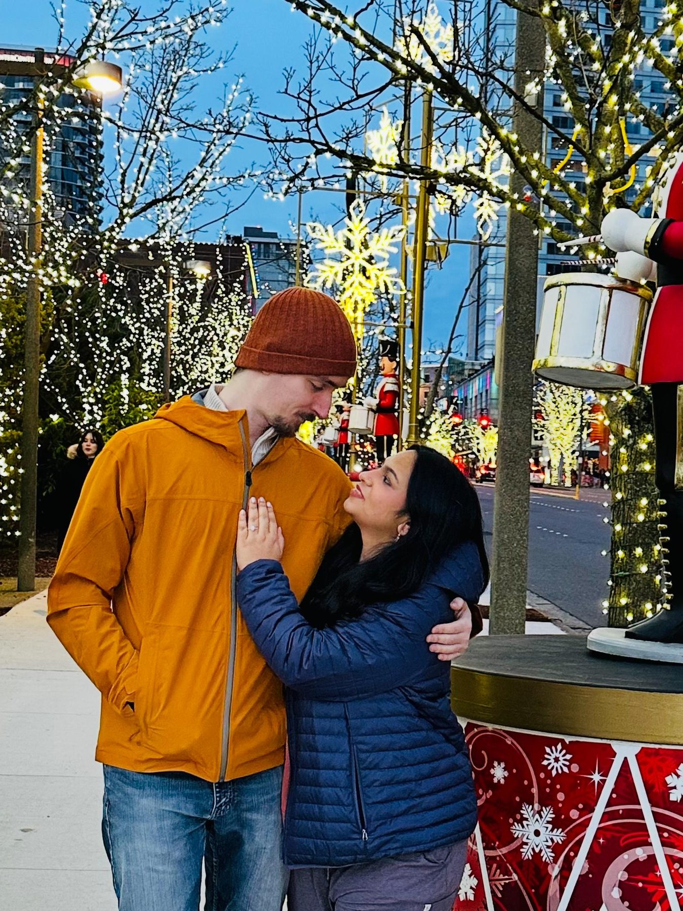 Prakriti and Mantas laughing together among downtown Christmas lights, beside a giant nutcracker